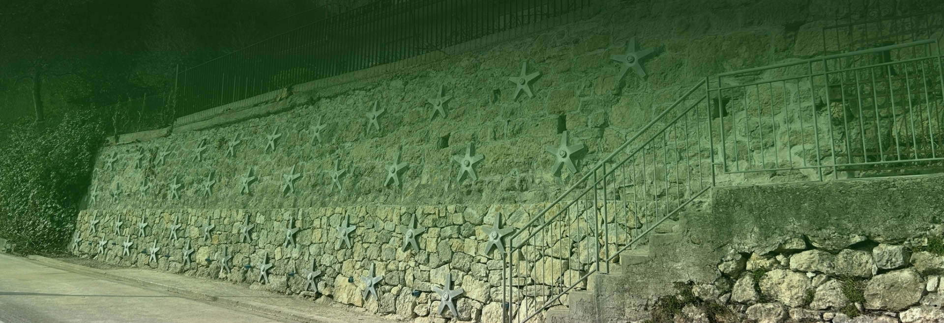 Muro in pietra lungo strada con ancoraggi a stella e corrimano