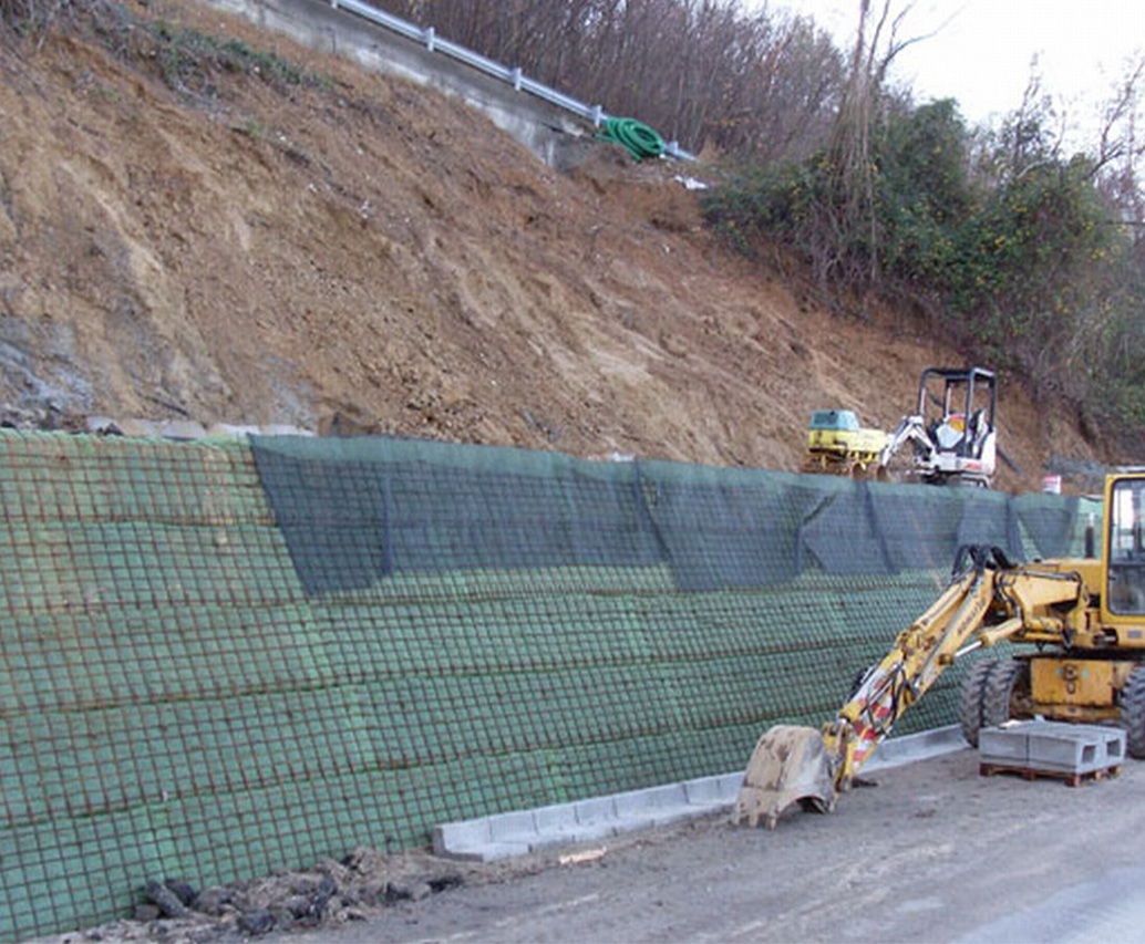 Pendio con rete geogrid e escavatore giallo