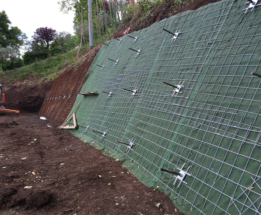 Pendio con rete verde e mini escavatore